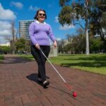 A person walking down a path outside using their cane.