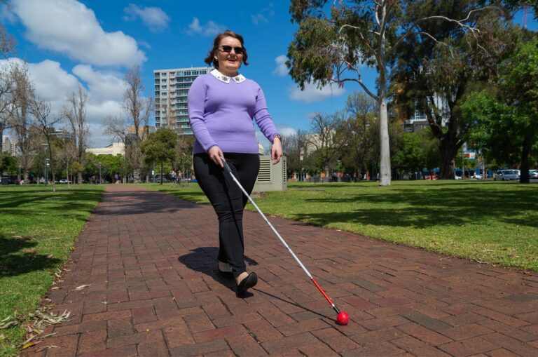 A person walking down a path outside using their cane.