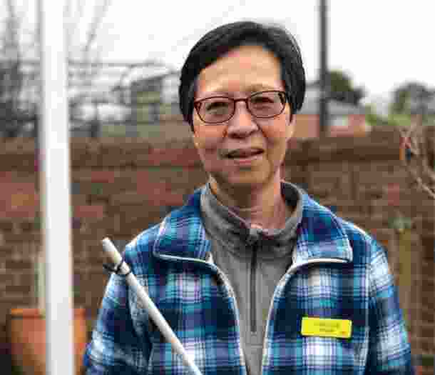 A person standing outside smiling at the camera while holding their white cane.