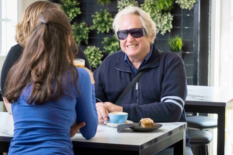 Three people seated at a cafe table. The one person who is facing the camera is smiling.