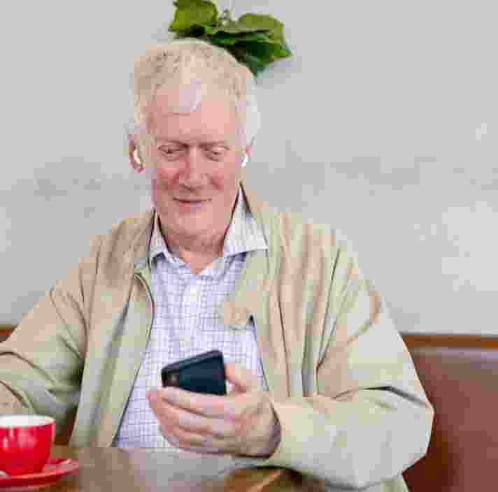 An older adult man sitting at a cafe looking at their phone.