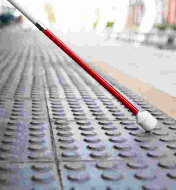 Close up image of the bottom half of a white cane on tactile tiles.