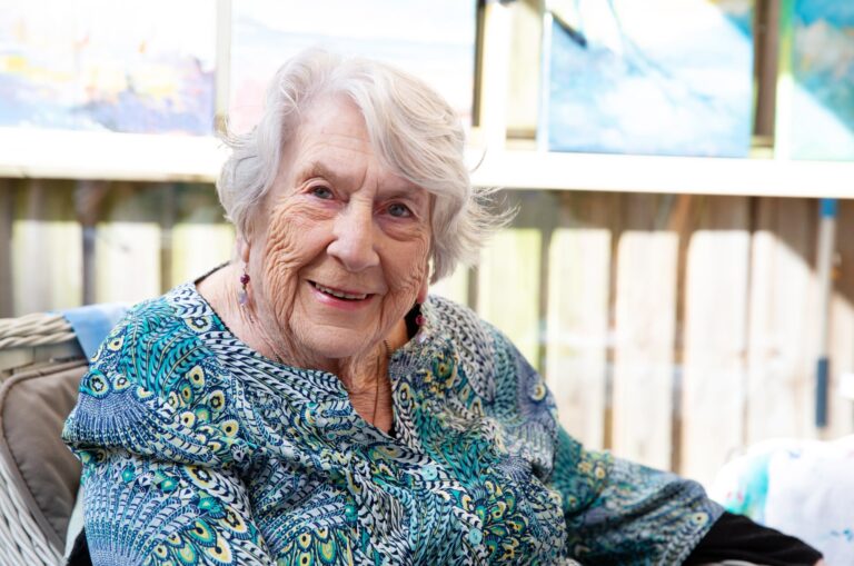 An older adult sitting in a chair smiling at the camera.