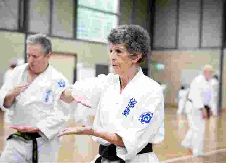 Two people at an indoor karate class. Both are in a karate uniform and are holding their hands in a karate pose.