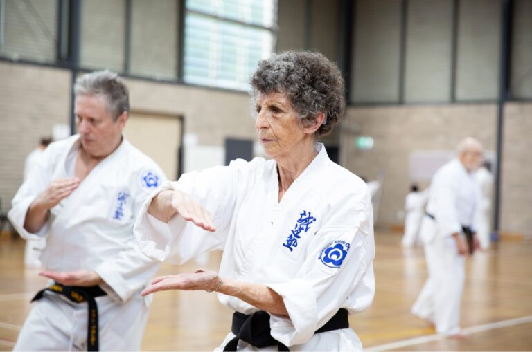Two people at an indoor karate class. Both are in a karate uniform and are holding their hands in a karate pose.