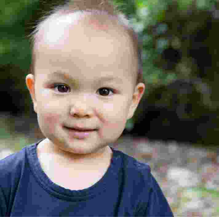 A young baby looking at the camera with a small smile on their face.