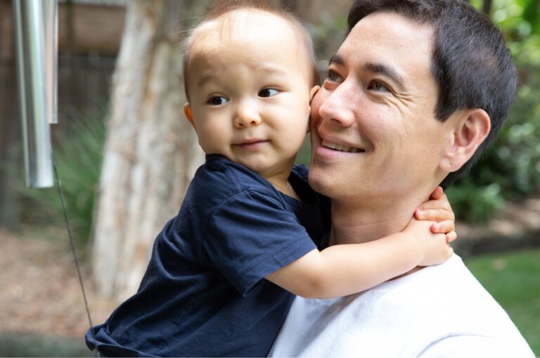 A father holding his toddler. The father has a smile on his face