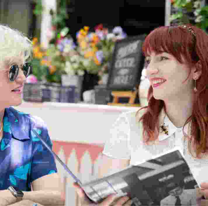 Two people sitting at a cafe looking at each other. They are both smiling and one is holding a menu.