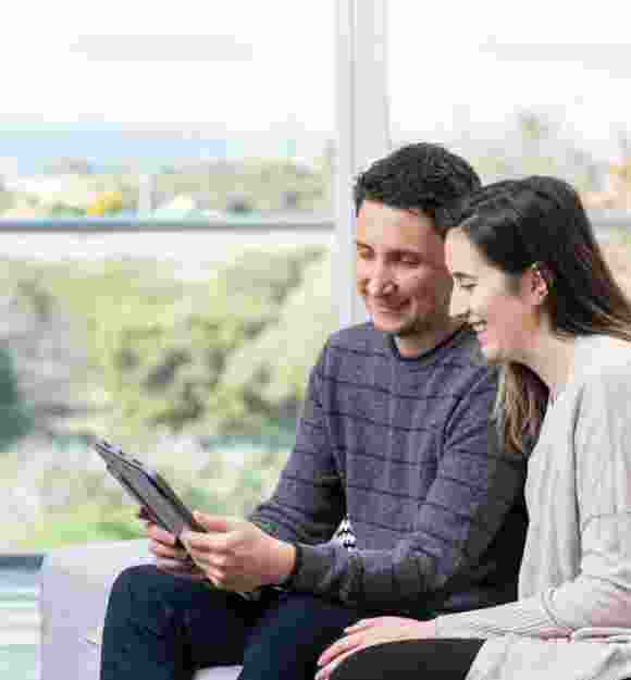 Two people sitting on a couch looking at a tablet together