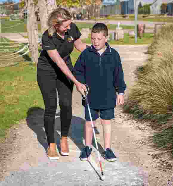 A Guide Dogs staff member assists a child using a white cane
