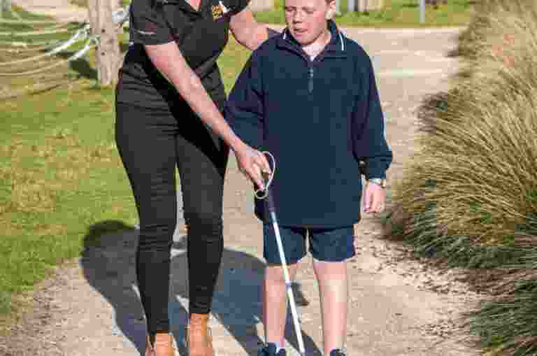A Guide Dogs staff member assists a child using a white cane