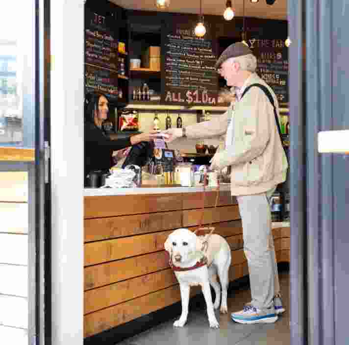 Allan and Guide dog Yoki ordering coffee at a cafe counter