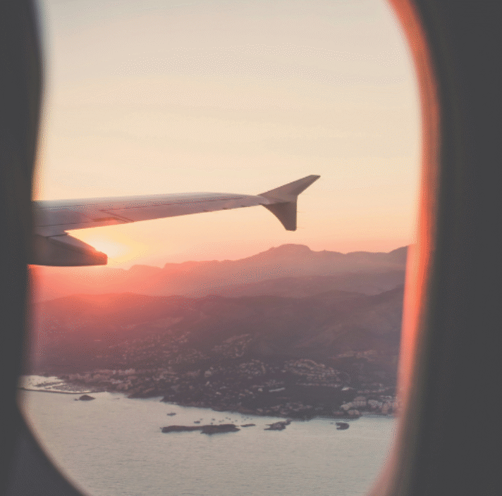 An aerial view of a mountainous coastal town at sunrise through a plane window, with part of the plane’s wing visible.