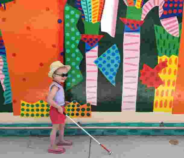 Stella holding her cane in front of a colourful mural