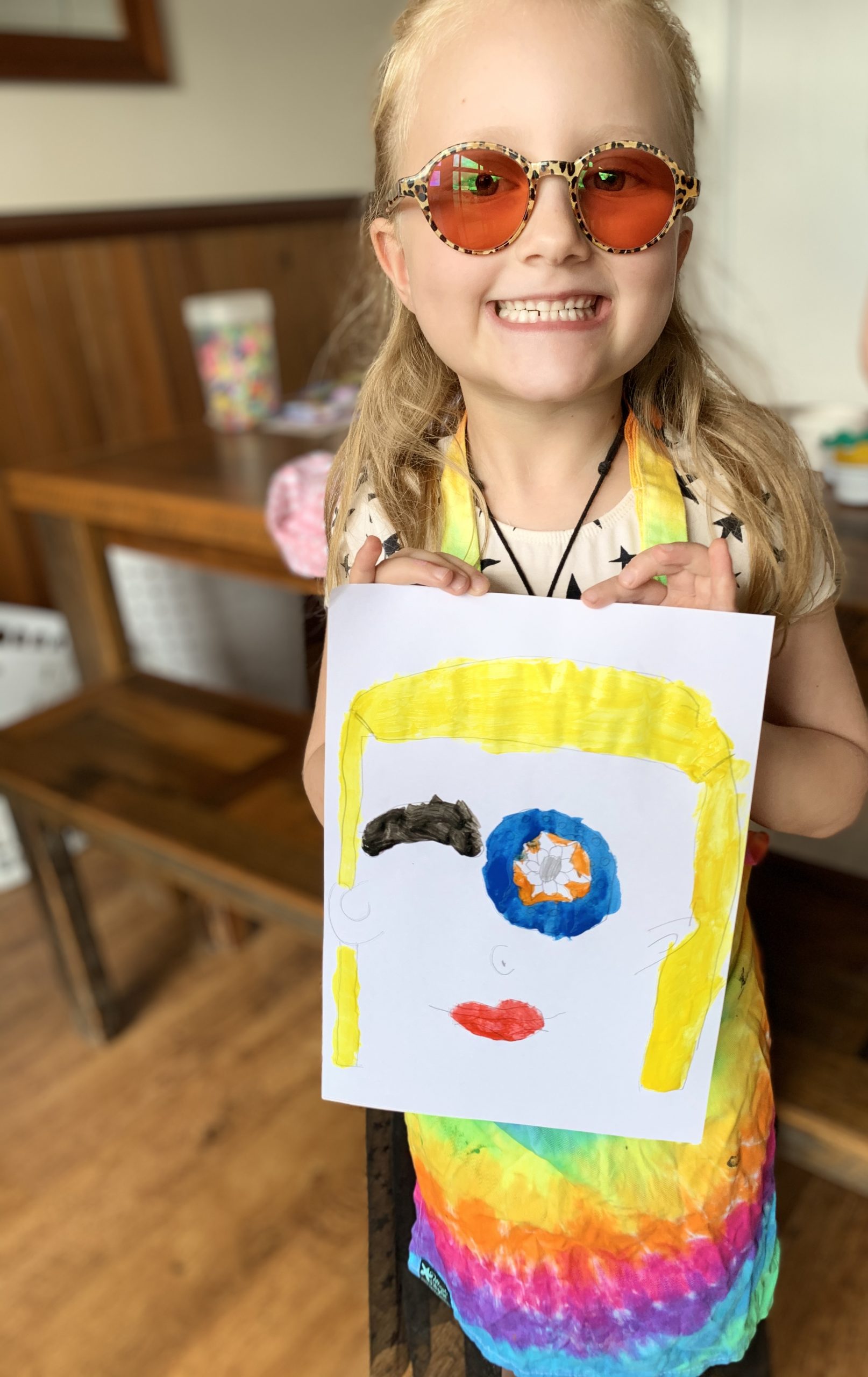 Stella smiling and holding up a painting that she has done