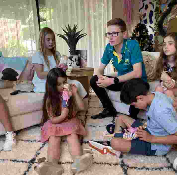 Jaryd Clifford sits on a couch surrounded by children who are playing with Kmart Inclusion dolls