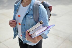 An image of a person (likely a student) with a backpack, carrying some books.
