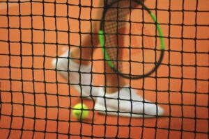 image of a tennis net, with a players legs and tennis racket visible through the net