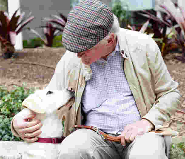 A man sitting outside looking at his Yellow Labrador guide dog