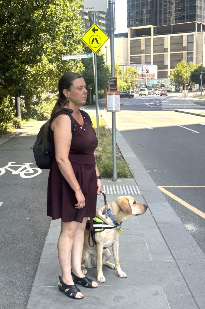 Paula Hobley and her Guide Dog, Kristin, waiting for an Uber at a kerbside.