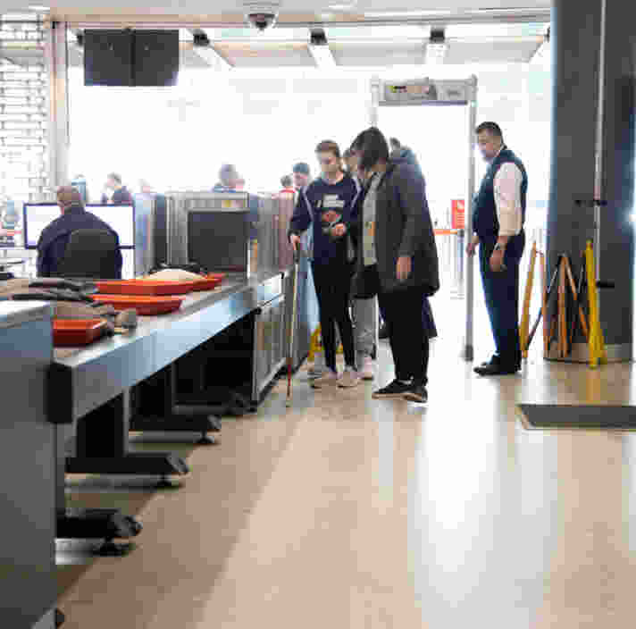 A white cane user walks past the baggage X-ray machine at airport security.
