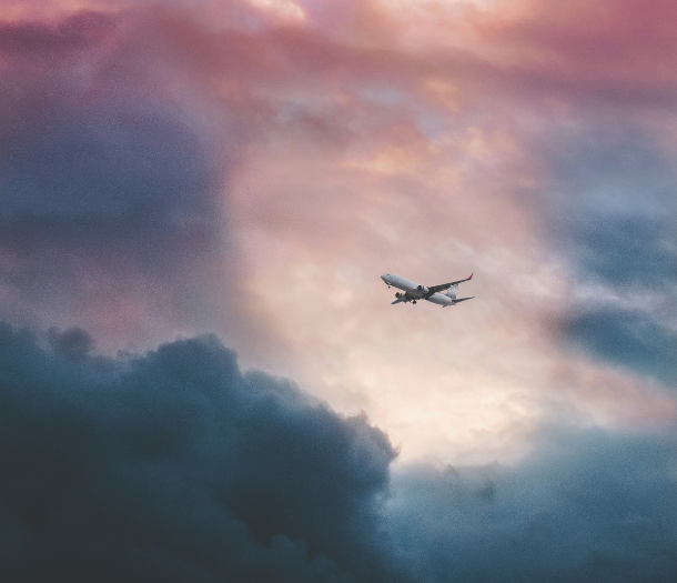 A plane flying through blue, purple, and pink clouds in the sky.