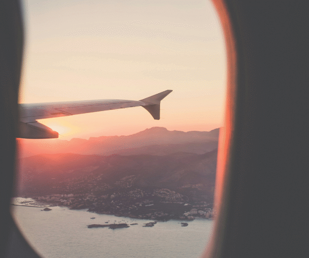 An aerial view of a mountainous coastal town at sunrise through a plane window, with part of the plane’s wing visible.