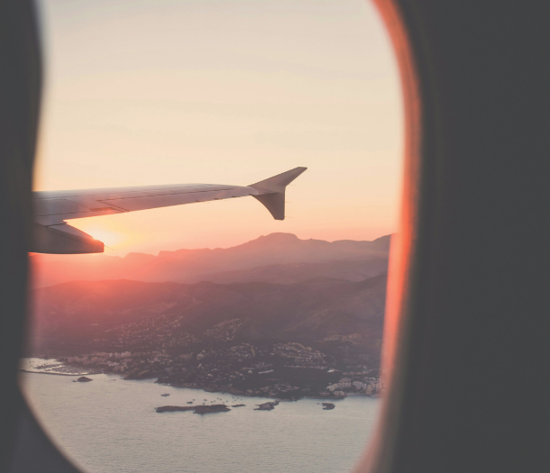 An aerial view of a mountainous coastal town at sunrise through a plane window, with part of the plane’s wing visible.