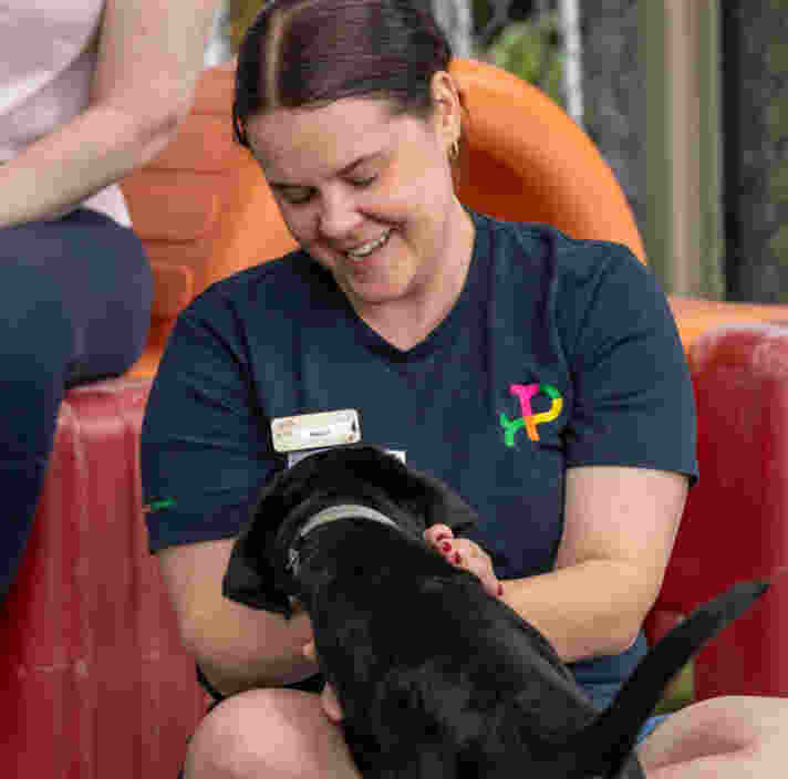 Petstock team member Sally sits on the ground patting black Labrador puppy Sully.
