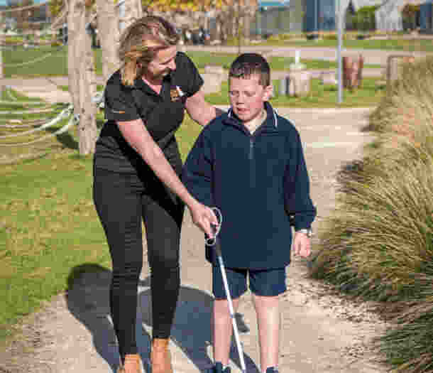A Guide Dogs staff member assists a child using a white cane