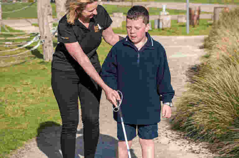 A Guide Dogs staff member assists a child using a white cane