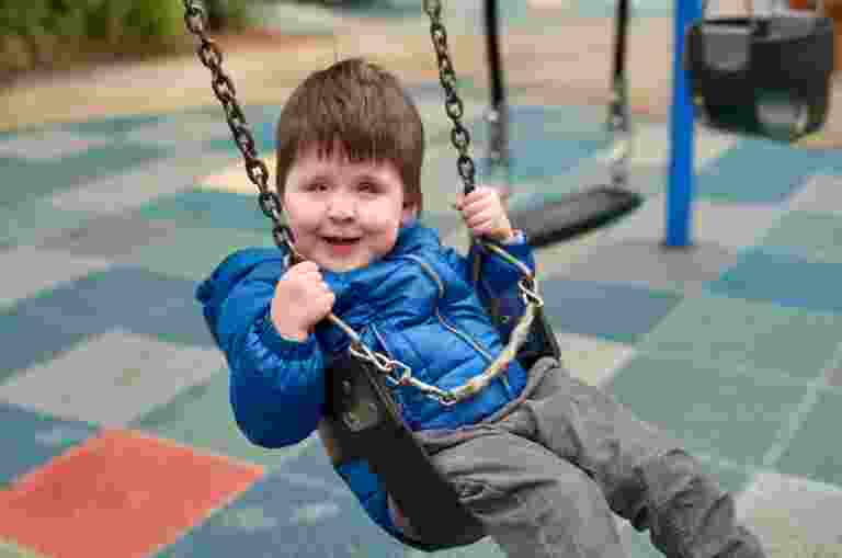 Boy wearing bright blue jacket on a swing