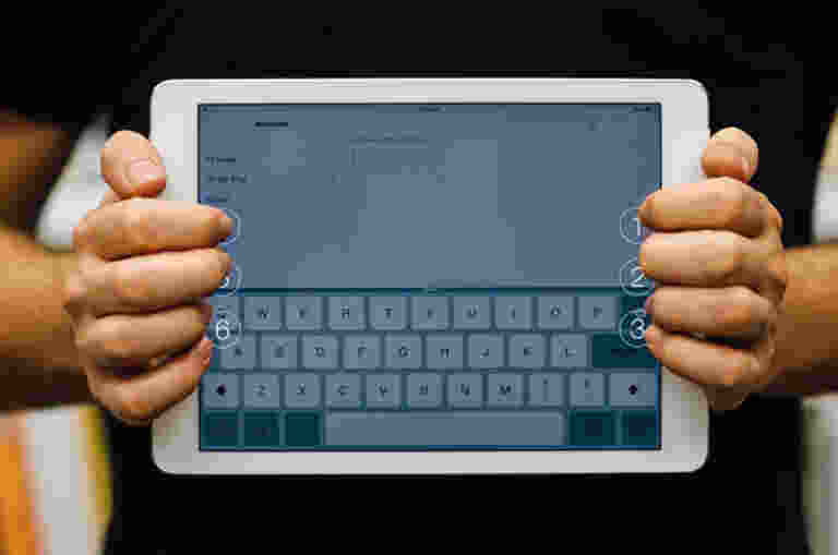 A person is holding an ipad. They are standing behind it, holding the device landscape with the screen to the camera