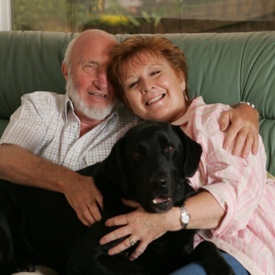 Bill and Isabel Patchett smiling with Companion Dog Galen the black Labrador