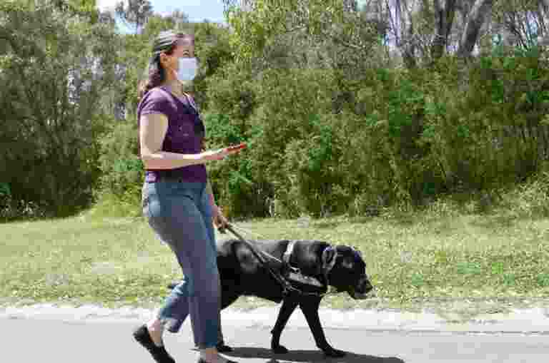 Guide Dog Handler Erin with black Guide Dog Jet walk through Jells Park. Erin is holding her mobile device using the BlindSquare app