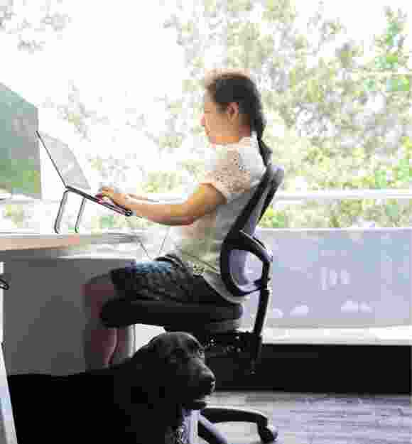 A person sitting at a desk using their laptop. The image is a profile view.