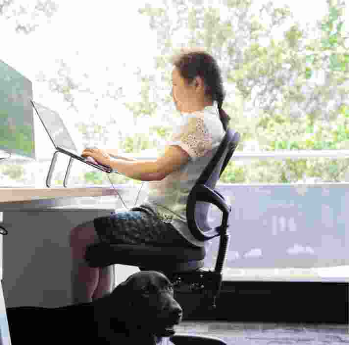 A person sitting at a desk using their laptop. The image is a profile view.