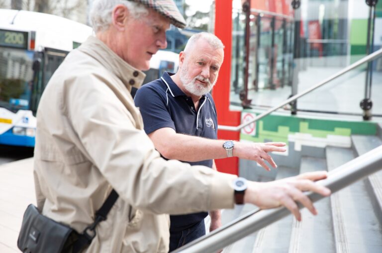 A Guide Dogs staff member assisting an an older adult with navigating a handrail.