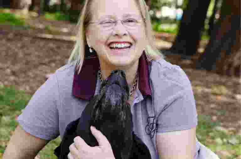 A person and their black labrador Guide Dog outside in the park. The dog is looking up at the person and the person is smiling at the camera.