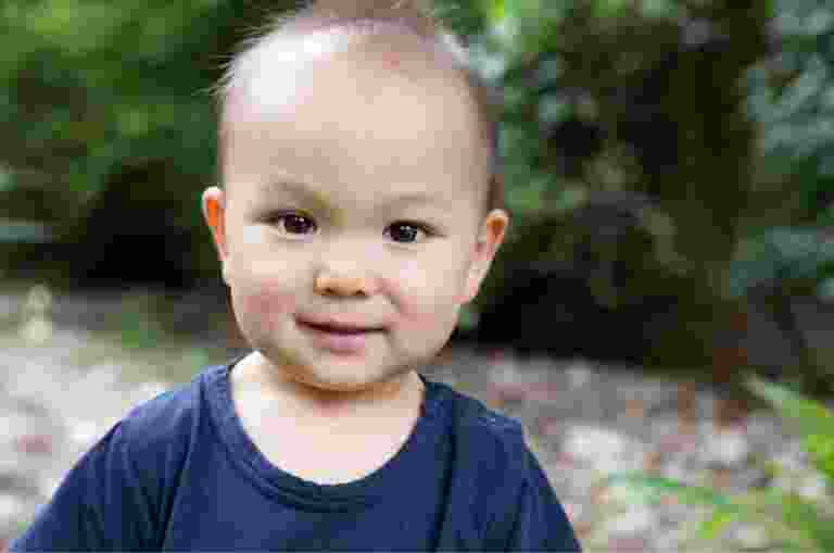 A young baby looking at the camera with a small smile on their face.