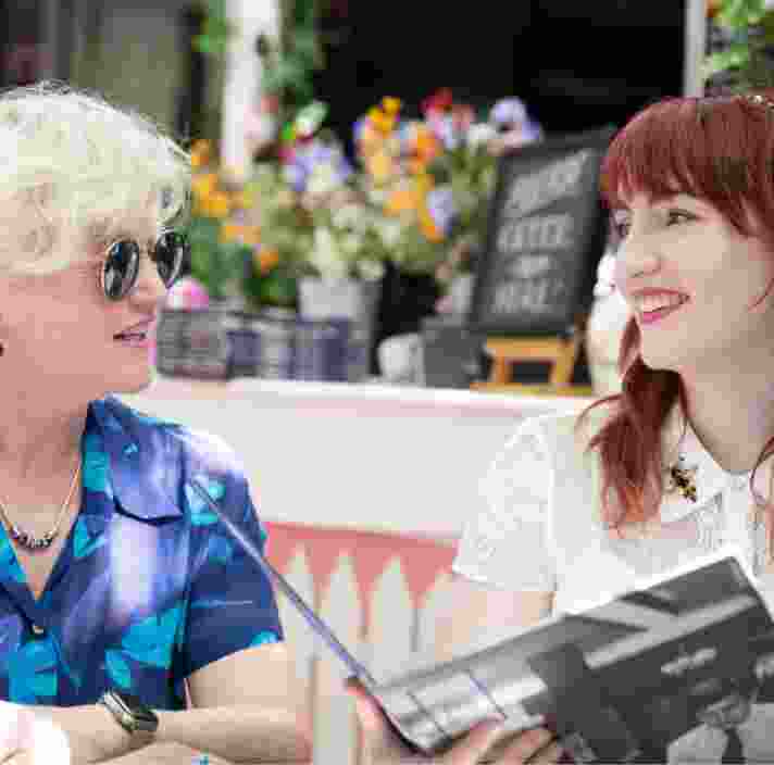 Two people sitting at a cafe looking at each other. They are both smiling and one is holding a menu.