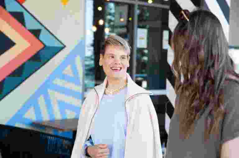 Two people looking at each other while they are walking down the street. One has their back to the camera while the other is smiling