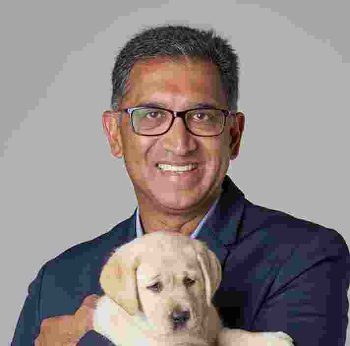 Headshot of Guide Dogs Victoria's Board Director, Harish Rao. Harish is looking at the camera smiling and holding a yellow eight week old labrador puppy.