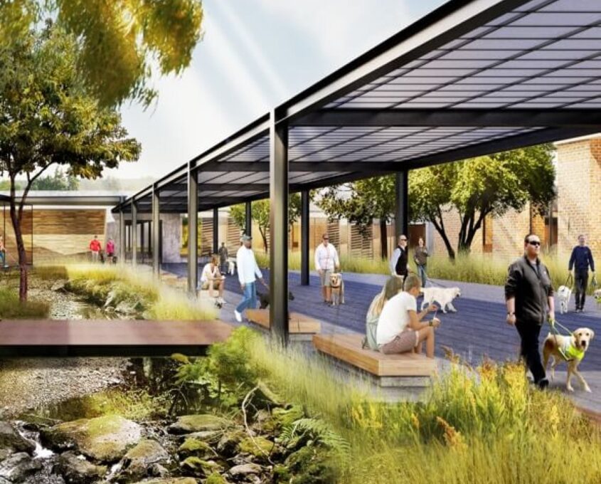 A render of a building with an outside footpath that is covered, next to a small stream with pebbles in it. Across the stream is a wooden bridge.