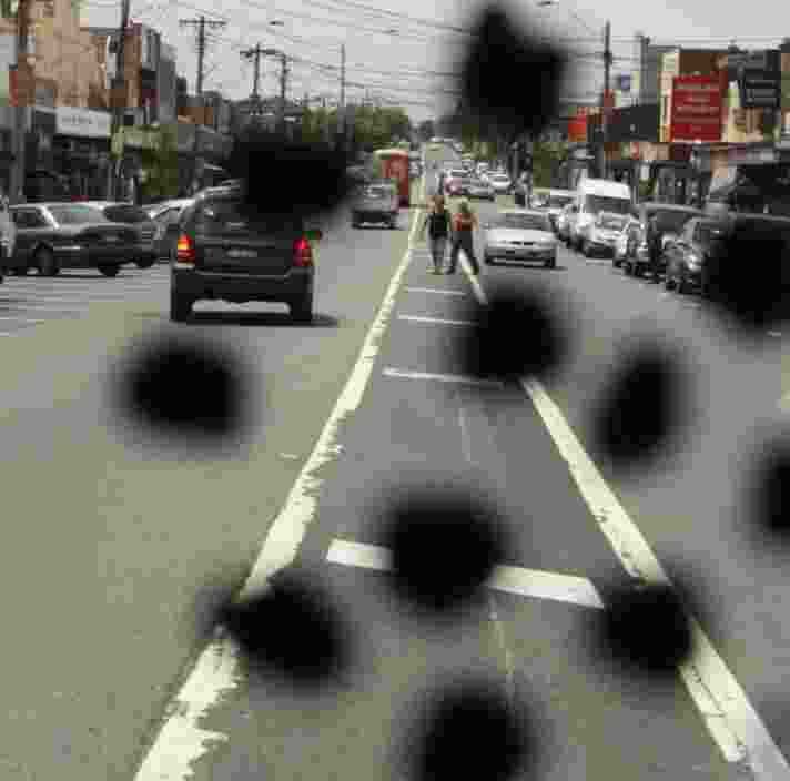 A busy road with cars on it. There are black spots on the image to portray how someone with diabetic retinopathy might view it.