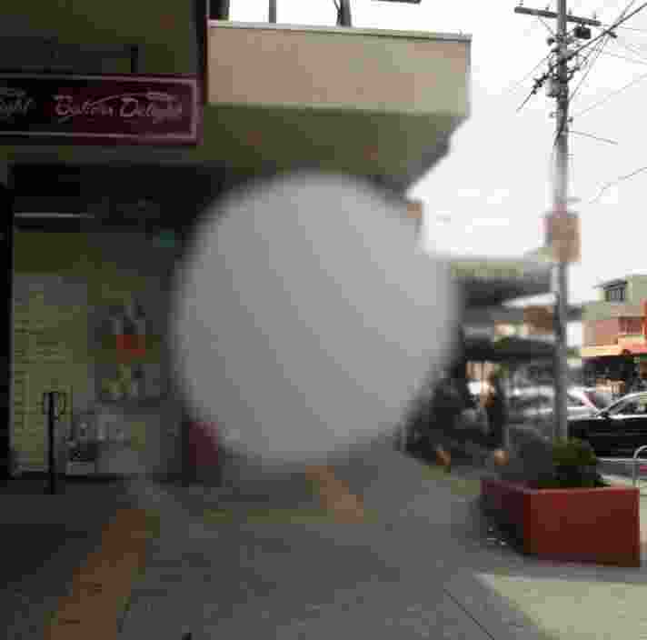 A busy footpath. The middle of the image is blurred with a white mark to portray how someone with macular degeneration might view it.