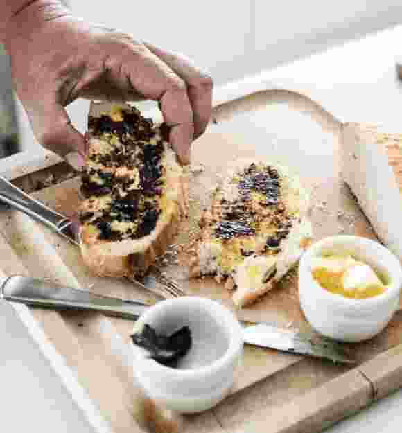 A person picking up a piece of buttered toast that is on a wooden board. There is a second piece of toast on the board