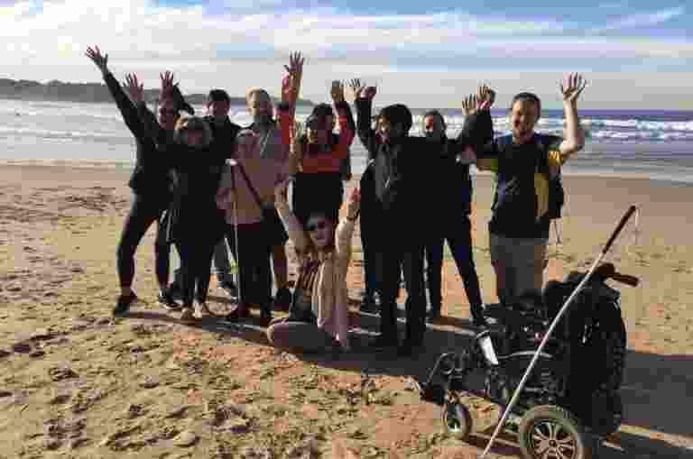 A group of people on a beach facing the camera with their arms in the air