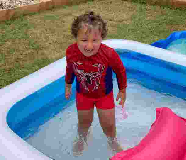 Ezra standing in an inflatable pool, smiling while wearing a Spiderman top