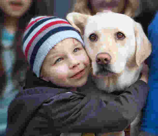 A young boy wearing a beanie, hugging a yellow Labrador.